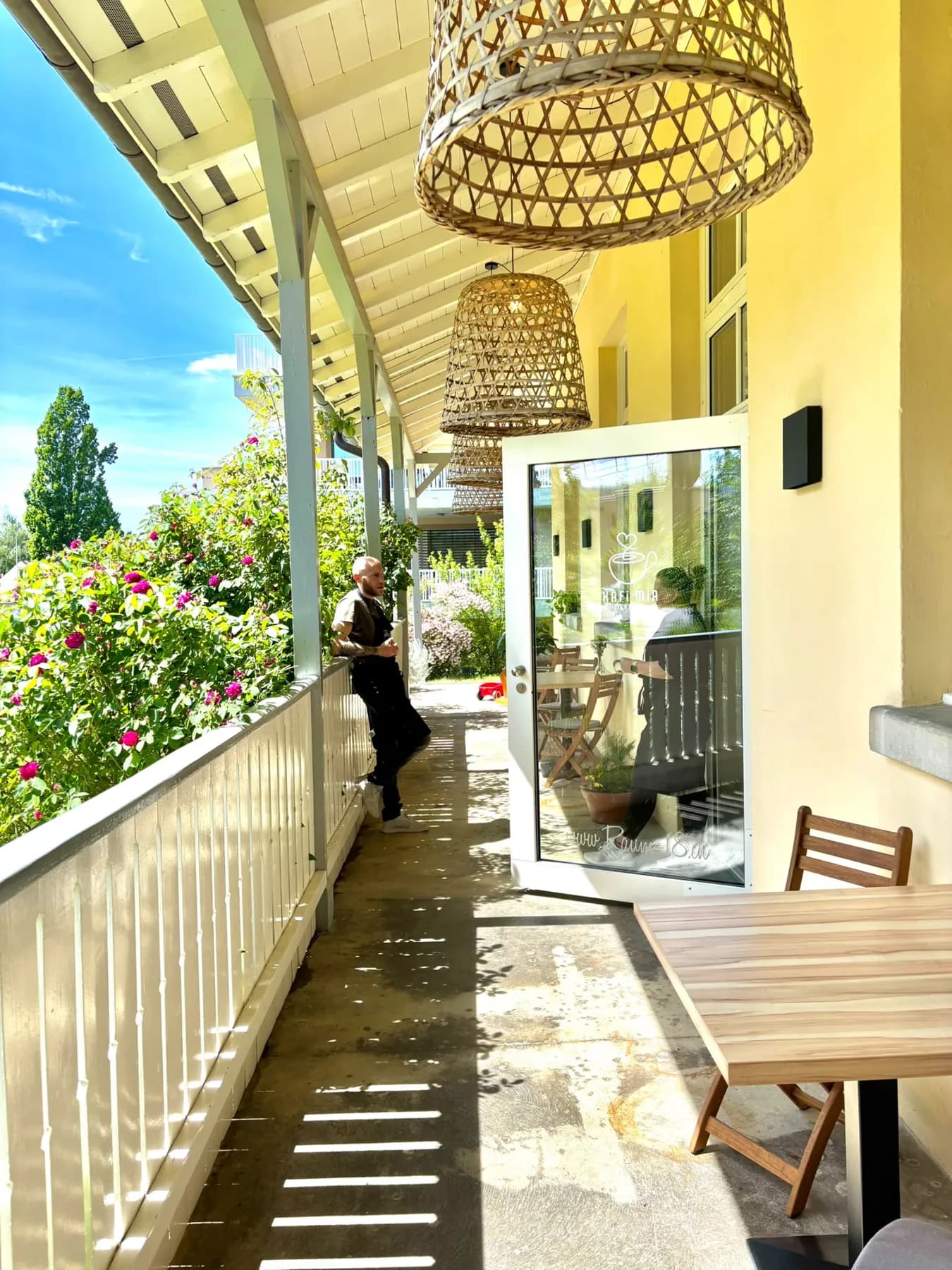 Sonnige Veranda des Kafi Mia mit Holztischen und Blick ins Grüne